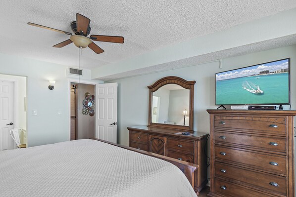 A bedroom with a bed, a dresser, a television, and a ceiling fan.