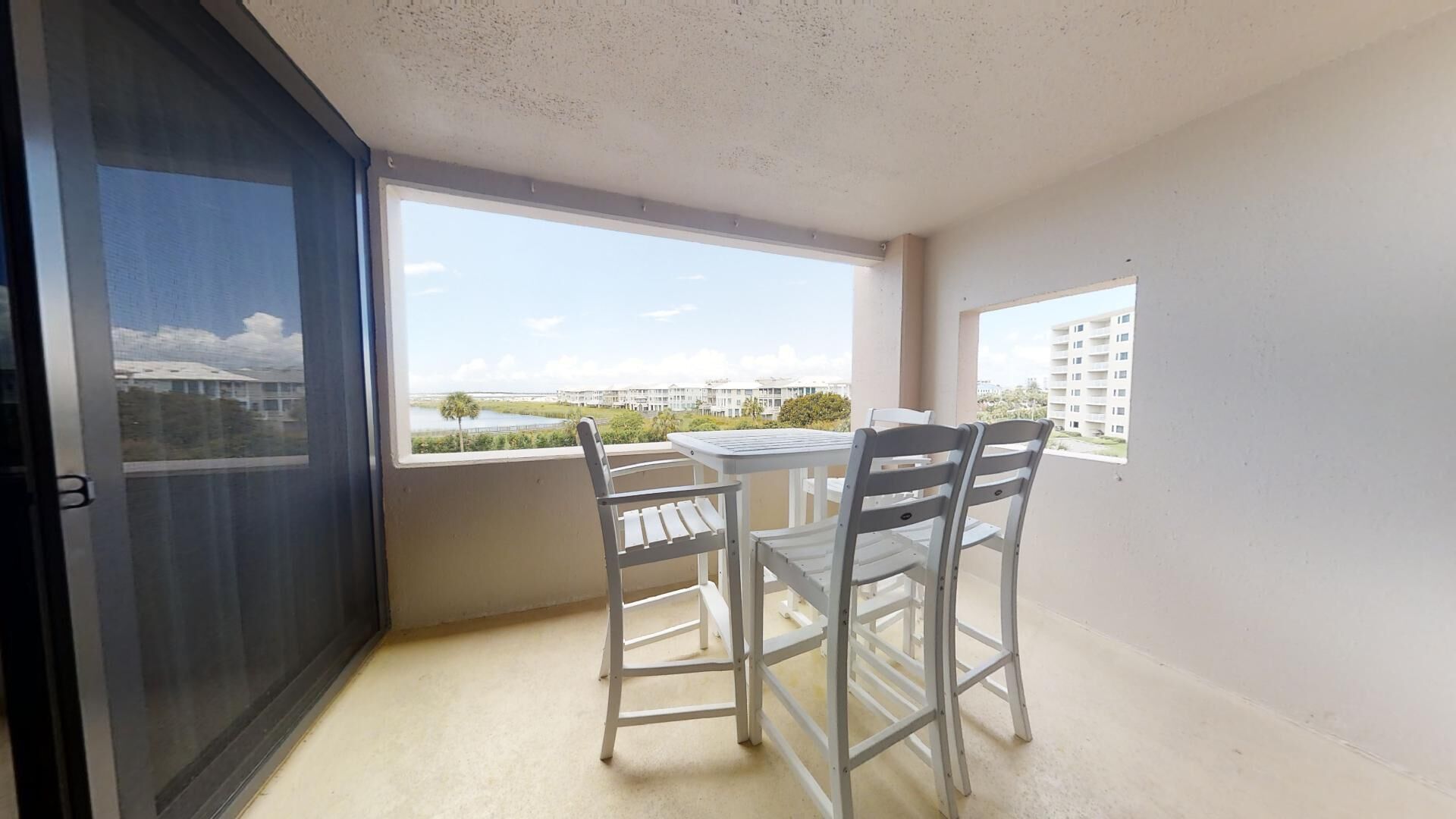 A balcony with a table and two chairs, overlooking a body of water and buildings.