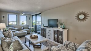 A living room with a sofa, ottoman, TV, and a decorative mirror. - Recently Updated, Comfortable and Spacious! Stunning Jetty Views at Jetty East! (Destin)