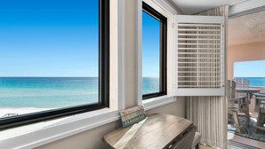 Una habitación con vistas al océano a través de amplios ventanales, un banco de madera y un ventilador de techo.