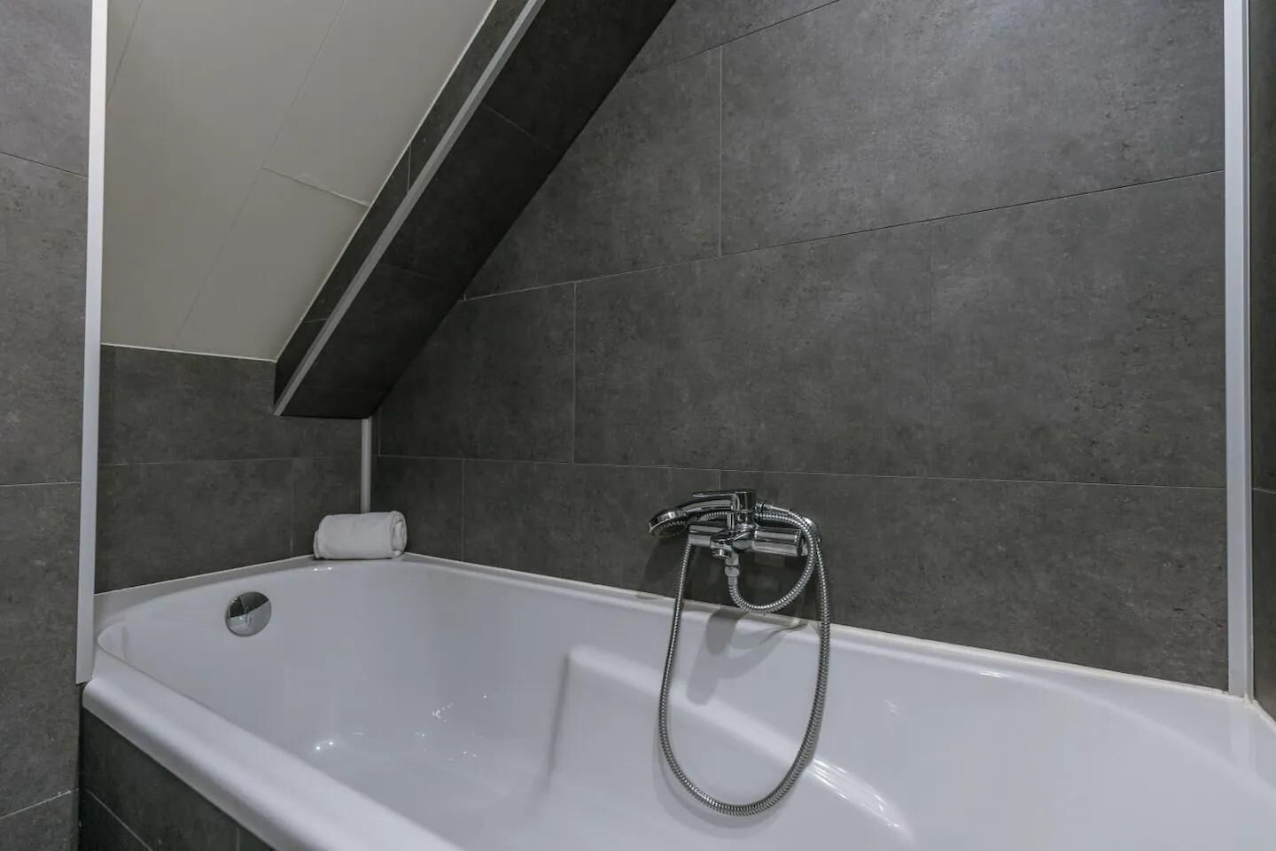Un bagno moderno con una vasca, una doccetta e un asciugamano.