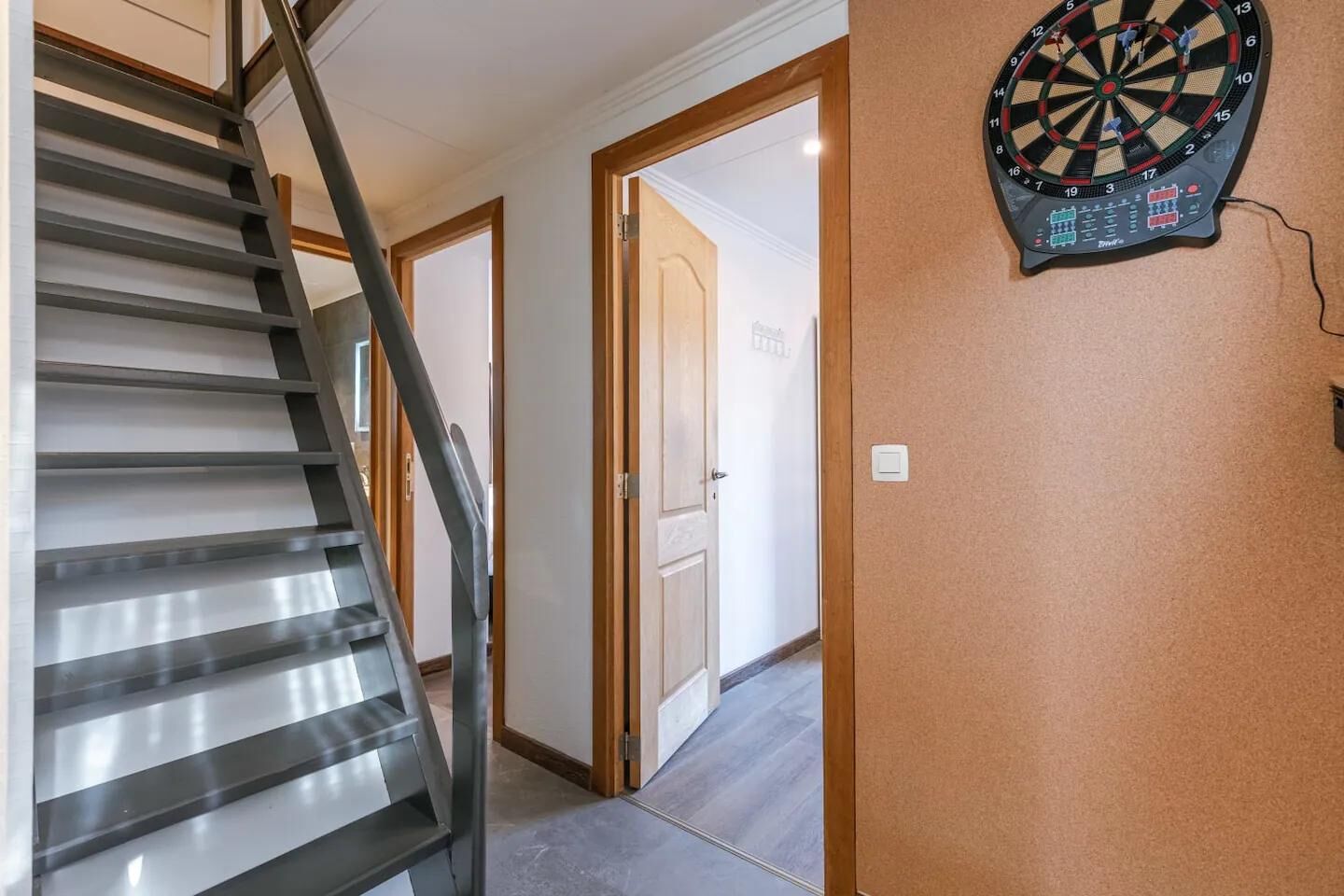 Una scala che porta a una porta, un bersaglio da freccette appeso al muro e un corridoio.