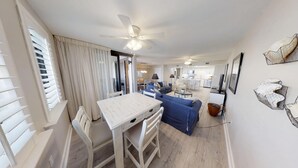 Een ruime woonkamer met een eettafel, een blauwe bank en een plafondventilator.