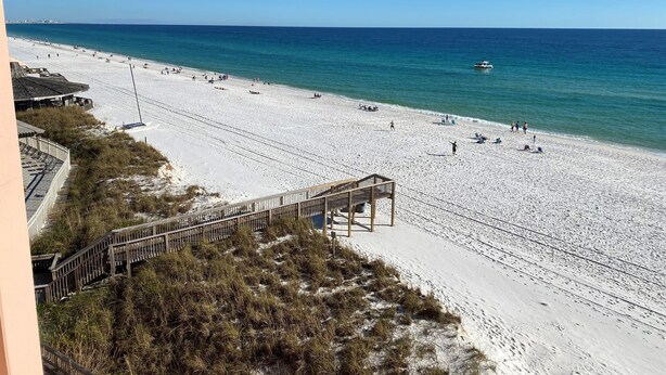 Ein Strand mit einer Holzpromenade, die zum Ufer führt, klarem blauen Wasser und einem entfernten Boot.