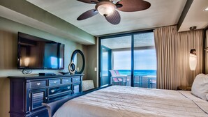 Habitación de hotel con una cama grande, un aparador, un televisor y vistas al océano a través de una puerta corrediza.