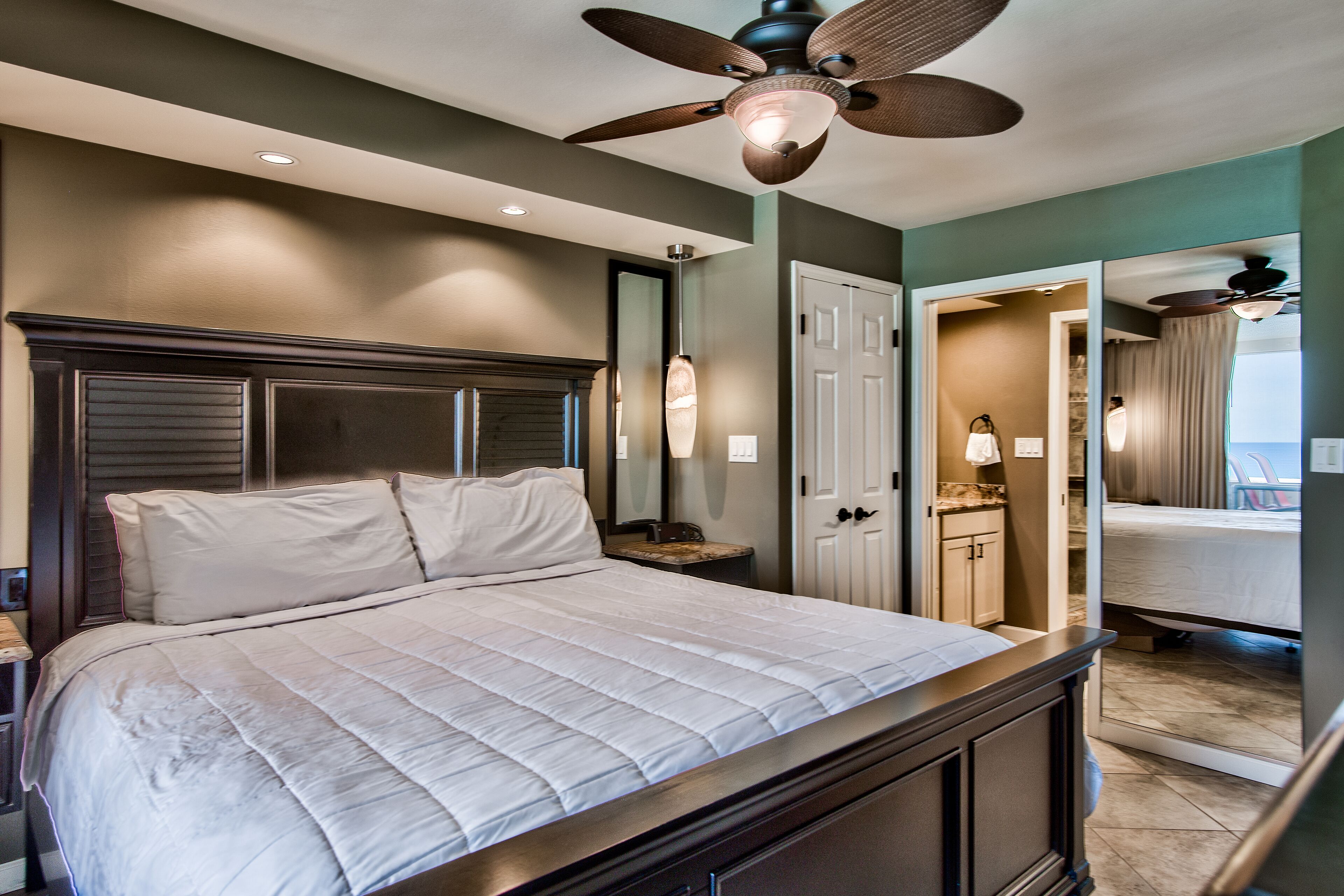 A bedroom with a large bed, a ceiling fan, a nightstand, a dresser, and a mirror.
