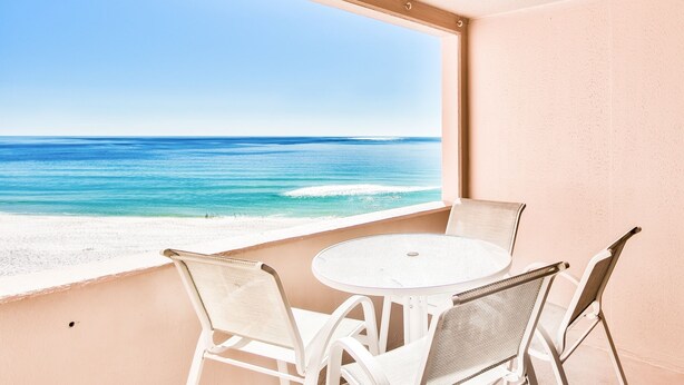 A balcony with a white table and chairs, overlooking a beach and ocean. - Gulf view at Jetty East! One beach chair set up daily. (Destin)