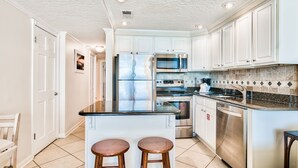 A modern kitchen with white cabinets, stainless steel appliances, and a central island with stools. - Gulf view at Jetty East! One beach chair set up daily. (Destin)