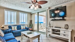 A living room with a sofa set, a coffee table, a TV, and a balcony with a view of the ocean. - Gulf view unit at Jetty East! One beach chair set up daily. (Destin)