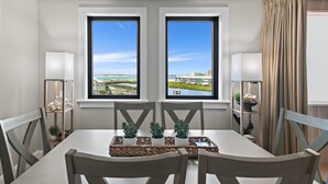 A dining area with a table, chairs, and a view of a cityscape through two windows. - Jetty view at Jetty East! One beach chair set up daily. (Destin)