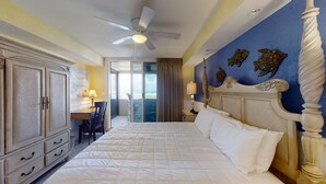 A hotel room with a large bed, a desk, and a view of the beach through the door.