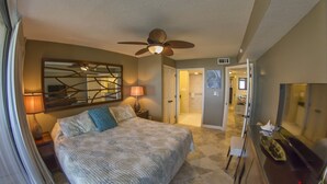 A bedroom with a bed, a ceiling fan, a nightstand, a lamp, a dresser, and a mirror.