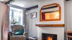 A cozy living room with a fireplace, a comfortable armchair, a large mirror, and a window with patterned curtains. - 2 bedroom accommodation in Shotley, Ipswich (Shotley, Ipswich)