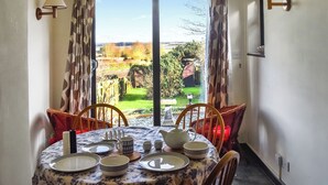 A dining area with a table set for four, a view of the garden through a large window, and two wall-mounted lamps. - 2 bedroom accommodation in Shotley, Ipswich (Shotley, Ipswich)