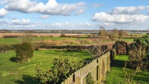 A rural landscape with a wooden fence, green fields, and a distant body of water under a partly cloudy sky. - 2 bedroom accommodation in Shotley, Ipswich (Shotley, Ipswich)