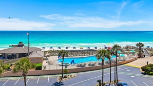 A pool area with a view of the ocean, a gazebo, and a parking lot with palm trees. - Spacious three-bedroom unit! One free beach chair set up daily. (Destin)