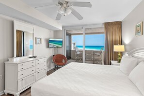 Habitación de hotel con cama, cómoda, silla, televisión, balcón y ventilador de techo, todo con vista al océano.