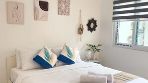 A neatly arranged bedroom with a bed, pillows, wall art, a mirror, and a window with blinds. - Sunset Paradise Moaboal (Moalboal)
