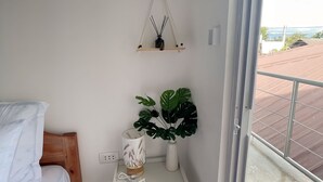 A bedroom with a bed, a bedside table with a lamp, a hanging plant, and a view of the outside balcony. - Sunset Paradise Moaboal (Moalboal)