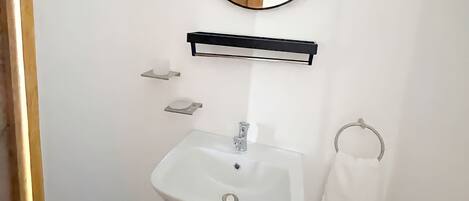 A bathroom with a white sink, a round mirror, and a towel rack.