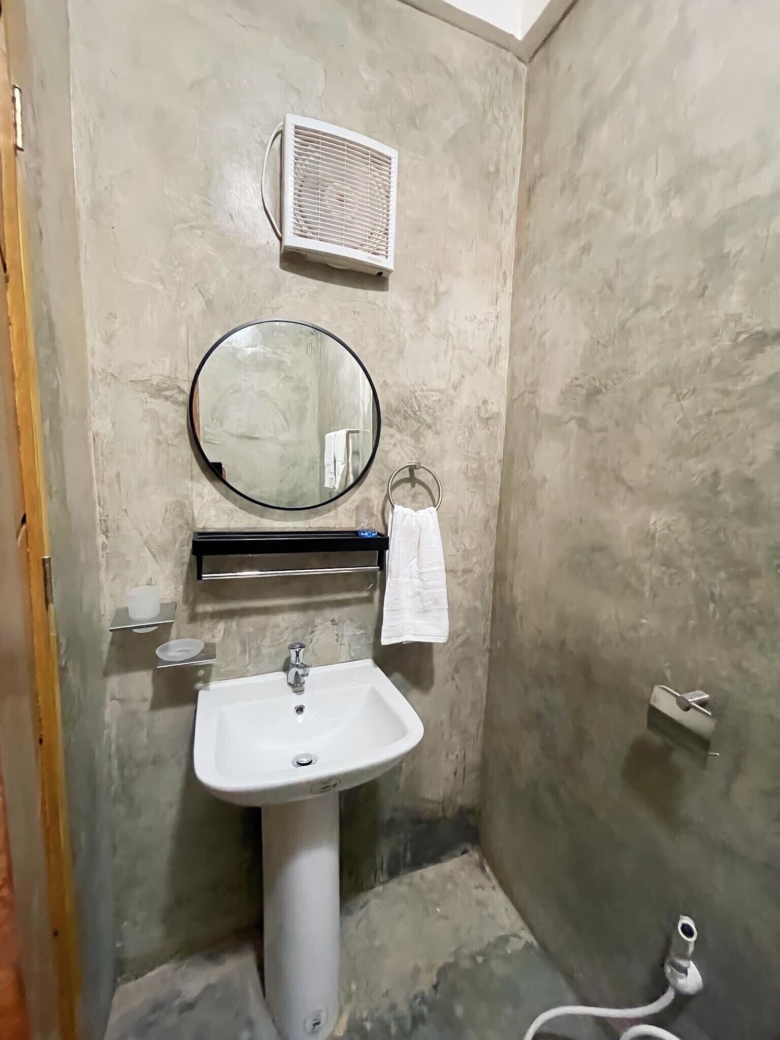 A bathroom with a white sink, a round mirror, a towel rack, and a wall-mounted air conditioner.
