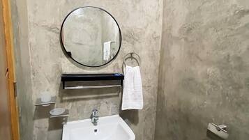 A bathroom with a white sink, a round mirror, a towel rack, and a wall-mounted air conditioner.