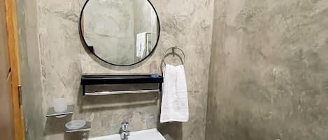 Un baño con un lavabo blanco, un espejo redondo, un perchero y un aire acondicionado de pared.