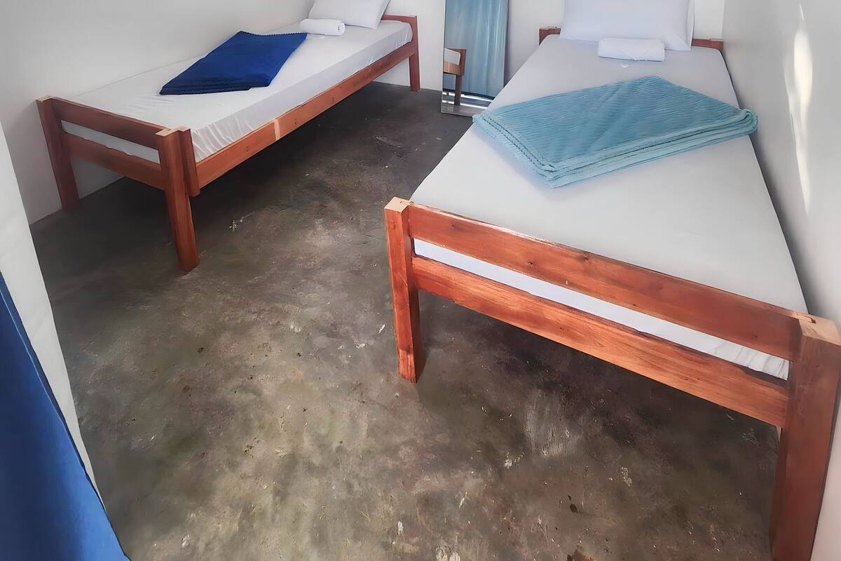 A room with two wooden beds, white walls, a ceiling fan, and a window.