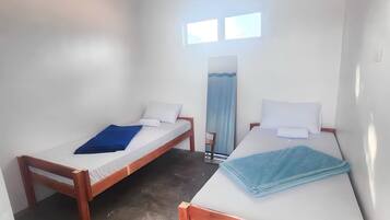 A room with two wooden beds, white walls, a ceiling fan, and a window.