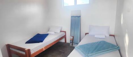 Una habitación con dos camas de madera, paredes blancas, ventilador de techo y una ventana.