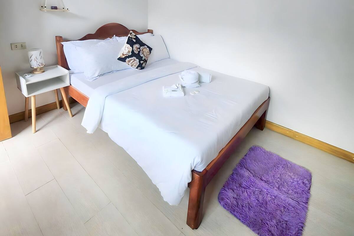 A neatly arranged bedroom with a bed, bedside table, and a purple rug.