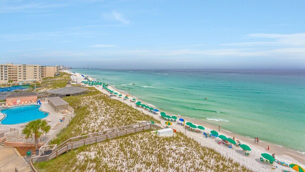 A beach resort with a swimming pool, beach umbrellas, and a boardwalk.