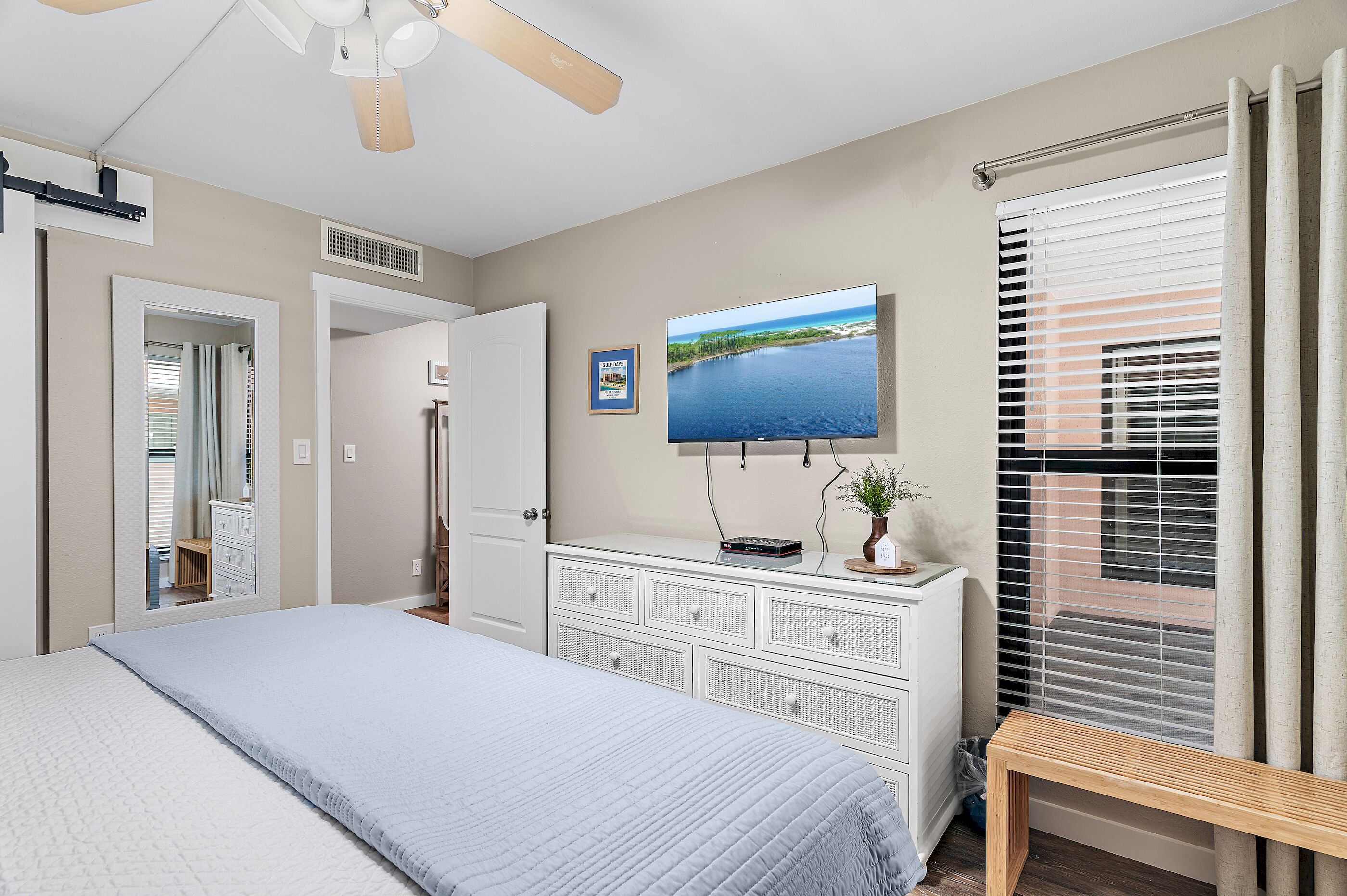 A bedroom with a bed, a dresser, a TV, a ceiling fan, and a window with blinds.