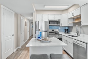 A modern kitchen with white cabinetry, stainless steel appliances, and a central island with seating.