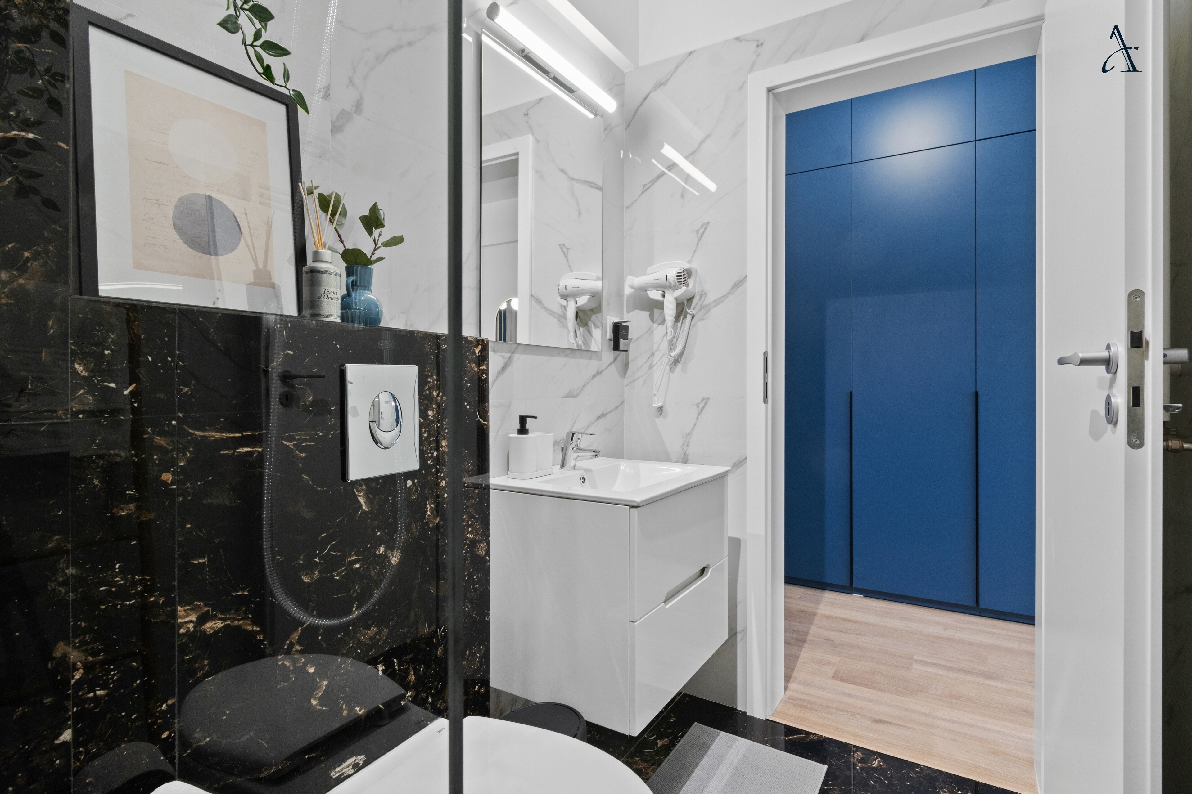 Ein modernes Badezimmer mit einem schwarzen Marmor-Waschtisch, einem weißen Waschbecken und einer blauen Tür.