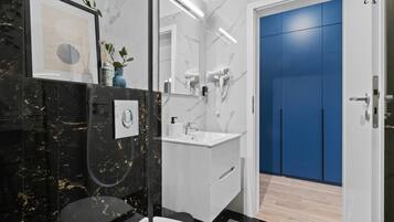 Ein modernes Badezimmer mit einem schwarzen Marmor-Waschtisch, einem weißen Waschbecken und einer blauen Tür.
