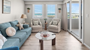 Ein modernes Wohnzimmer mit einer Couch, Sesseln, einem Couchtisch und großen Fenstern mit Meerblick.