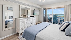 Ein Schlafzimmer mit Bett, Kommode, Fernseher und einem Balkon mit Stühlen.