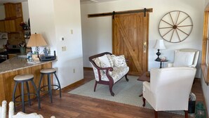 A modern kitchen with wooden cabinets, a bar area with stools, a large wooden door, and a round wall decoration.