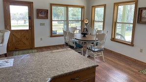 A kitchen with a granite countertop, wooden cabinets, and a dining area with white chairs and a table.