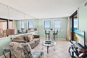 A living room with a sofa, armchair, coffee table, TV, and dining area with chairs and table. - Sunrise gulf view/beach front condo! Enjoy one free beach chair set up each day (Destin)