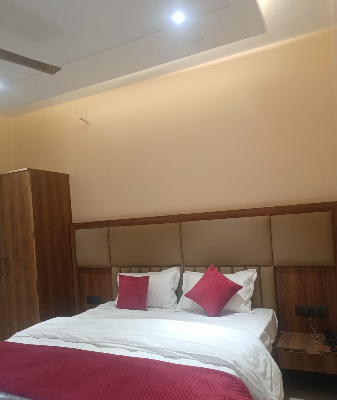 Una habitación de hotel con cama, armario de madera y cabecera con almohadas.