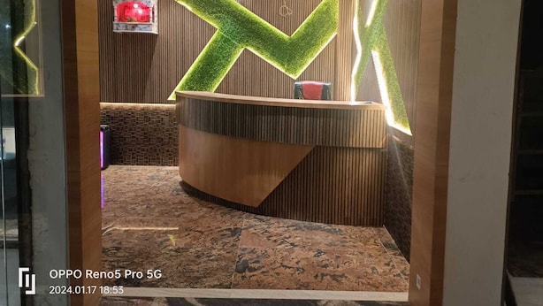 Un espace d'accueil avec un comptoir en bois, un panneau « X » vert et lumineux, et un petit objet rouge accroché au mur.