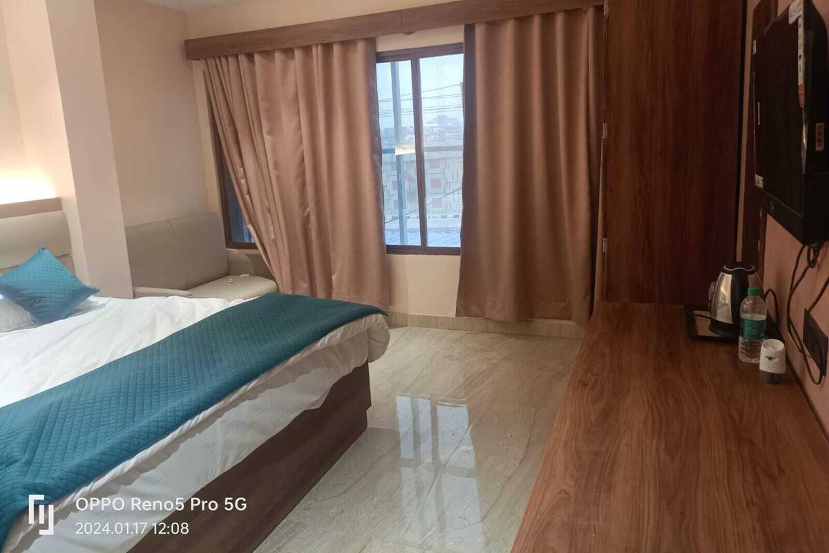 A hotel room with a bed, a desk, a chair, a ceiling fan, a window with curtains, and a television.