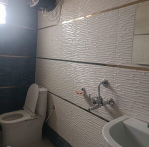 A bathroom with a textured wall, a toilet, a sink, and a shower head. - MR JAISWAL DHARMSHALA (Sultanpur)