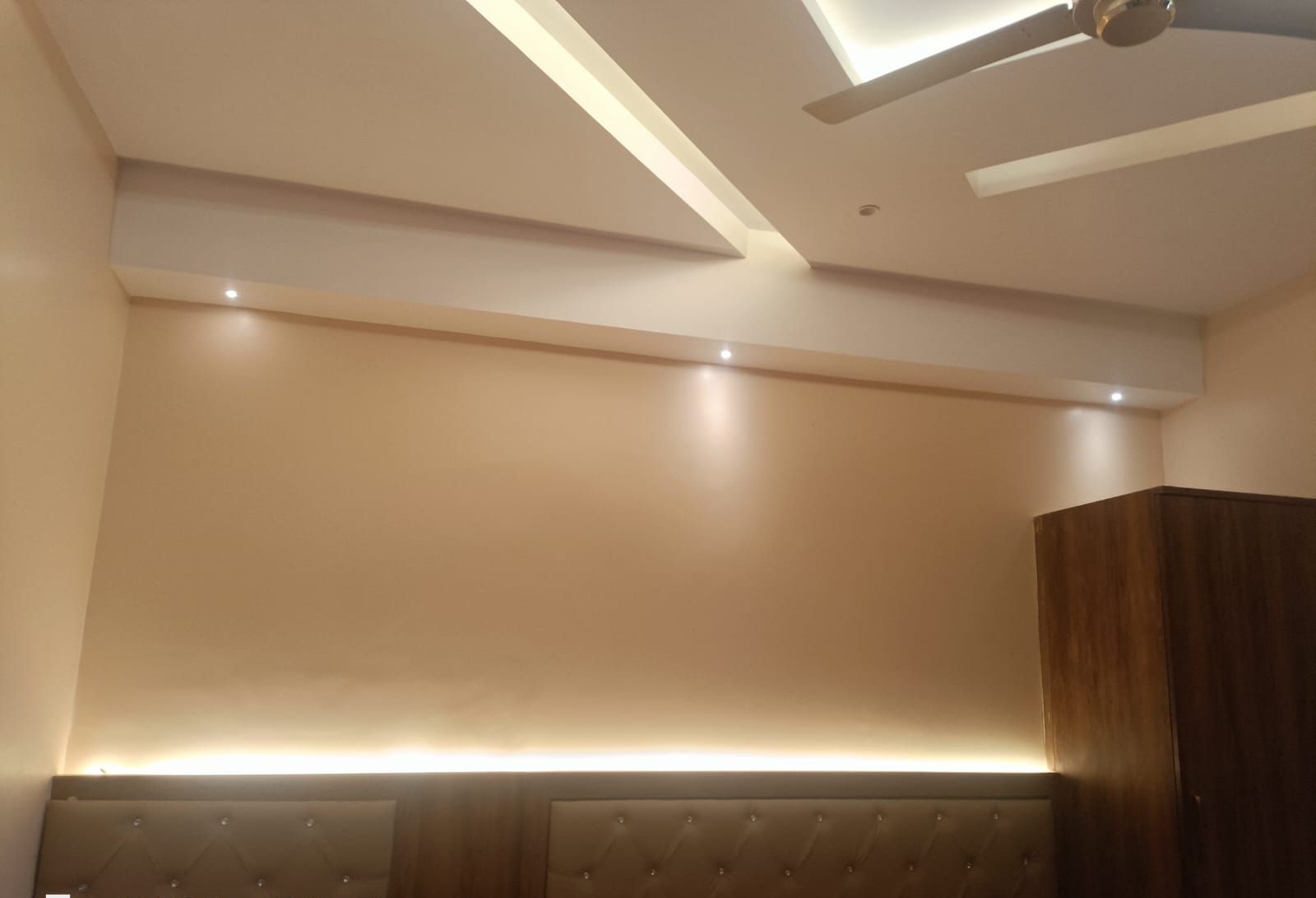 Un dormitorio moderno con cabecera capitonada, luces empotradas en el techo y un ventilador de techo.
