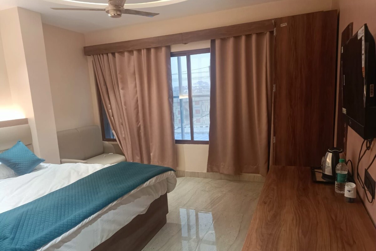 Habitació d'hotel amb llit, escriptori, cadira, ventilador de sostre, finestra amb cortines i televisió.