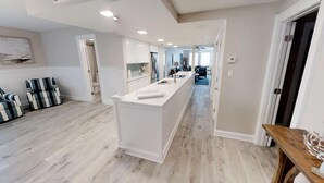A modern kitchen with white cabinetry, a central island, and a dining area with striped chairs.