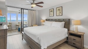Een slaapkamer met een groot bed, een plafondventilator, een nachtkastje met lamp en uitzicht op de oceaan door een schuifdeur.