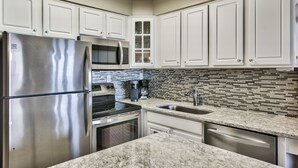 A modern kitchen with white cabinets, stainless steel appliances, a tiled backsplash, and granite countertops. - Sunset Jetty View! Enjoy one free beach chair set up and umbrella each day! (Destin)